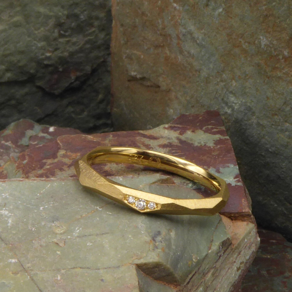 ein-ganz-schmaler-ring-mit-vielen-unregelmaessigen-facetten-beziehungsweise-polygonen-flaechen-der-ring-ist-ca-zweieinhalb-millimeter-breit-und-besteht-aus-gelbgold-er-ist-auch-in-fairtrade-gold-erhaeltlich-auf-einer-facette-sind-vollflaechig-drei-brillanten-eingefasst-ein-design-ehering-oder-verlobungsring-der-nicht-von-der-stange-ist-die-ringe-werden-von-hand-in-unserer-goldschmiede-in-frankfurt-am-main-angefertigt-alexandra-baum-schmuck