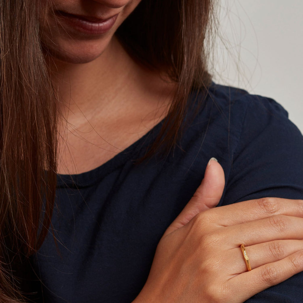 ein-am-finger-getragener-ganz-schmaler-ring-aus-unserer-ecken-und-kanten-kollektion-mit-vielen-unregelmaessigen-facetten-beziehungsweise-polygonen-flaechen-der-ring-ist-ca-zweieinhalb-millimeter-breit-und-besteht-aus-gelbgold-er-ist-auch-in-fairtrade-gold-erhaeltlich-auf-einer-facette-sind-vollflaechig-drei-brillanten-eingefasst-ein-design-trauring-oder-verlobungsring-der-nicht-von-der-stange-ist-die-ringe-werden-von-hand-in-unserer-goldschmiede-in-frankfurt-am-main-angefertigt-alexandra-baum-schmuck