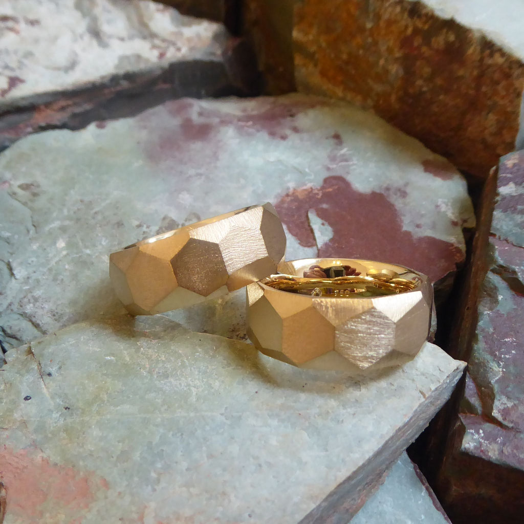 ein-paar-breite-rockige-ringe-mit-vielen-unregelmaessigen-facetten-oder-polygonen-flaechen-die-ringe-sind-ca-achteinhalb-millimeter-breit-und-bestehen-aus-fairtrade-gelbgold-geeignet-als-trauringe-oder-schmuckringe-fuer-menschen-die-auffaellige-ringe-moegen-die-ringe-werden-von-hand-in-unserer-goldschmiede-in-frankfurt-am-main-angefertigt-und-sind-individuell-anpassbar-alexandra-baum-schmuck