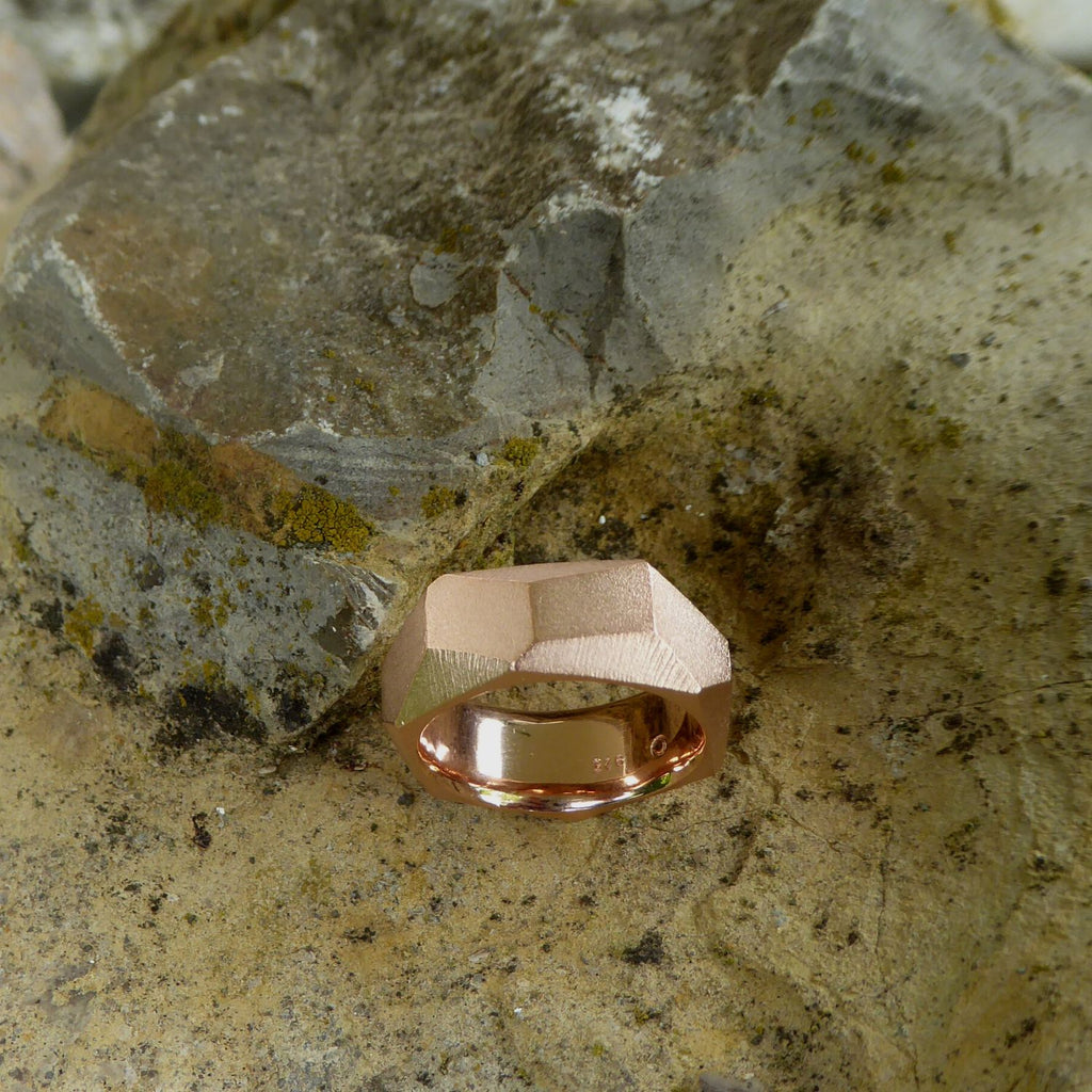 ein-breiter-auffaelliger-ring-mit-vielen-unregelmaessigen-facetten-oder-polygonen-flaechen-der-ring-ist-ca-achteinhalb-millimeter-breit-und-besteht-aus-rotgold-geeignet-als-trauring-oder-schmuckring-fuer-menschen-die-auffaellige-ringe-moegen-die-ringe-werden-von-hand-in-unserer-goldschmiede-in-frankfurt-am-main-angefertigt-und-sind-individuell-anpassbar-alexandra-baum-schmuck