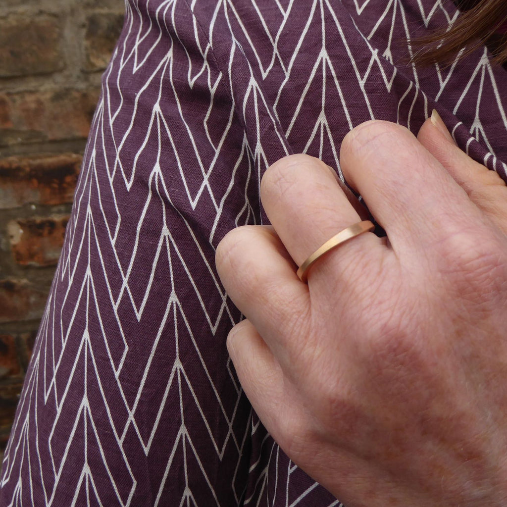 am-der-hand-getragener-ehering-mit-dem-namen-durch-dick-und-duenn-der-ring-besteht-aus-rosegold-die-form-ist-klassisch-aber-leicht-unregelmaessig-an-manchen-stellen-dicker-an-manchen-stellen-duenner-ein-design-trauring-der-sich-von-der-masse-abhebt-die-ringe-werden-von-hand-in-unserer-goldschmiede-in-frankfurt-am-main-angefertigt