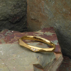 ein-ganz-schmaler-ring-mit-vielen-unregelmaessigen-facetten-beziehungsweise-polygonen-flaechen-der-ring-ist-ca-zweieinhalb-millimeter-breit-und-besteht-aus-gelbgold-er-ist-auch-in-fairtrade-gold-erhaeltlich-auf-einer-facette-sind-vollflaechig-drei-brillanten-eingefasst-ein-design-ehering-oder-verlobungsring-der-nicht-von-der-stange-ist-die-ringe-werden-von-hand-in-unserer-goldschmiede-in-frankfurt-am-main-angefertigt-alexandra-baum-schmuck