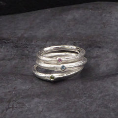 drei-aufeinander-gestapelte-astringe-mit-farbigen-brillanten-der-unterste-ring-hat-einen-grünen-dermittlere-ring-einen-blauen-und-der-oberste-einen-pinken-stein-im-blattansatz-eingefasst