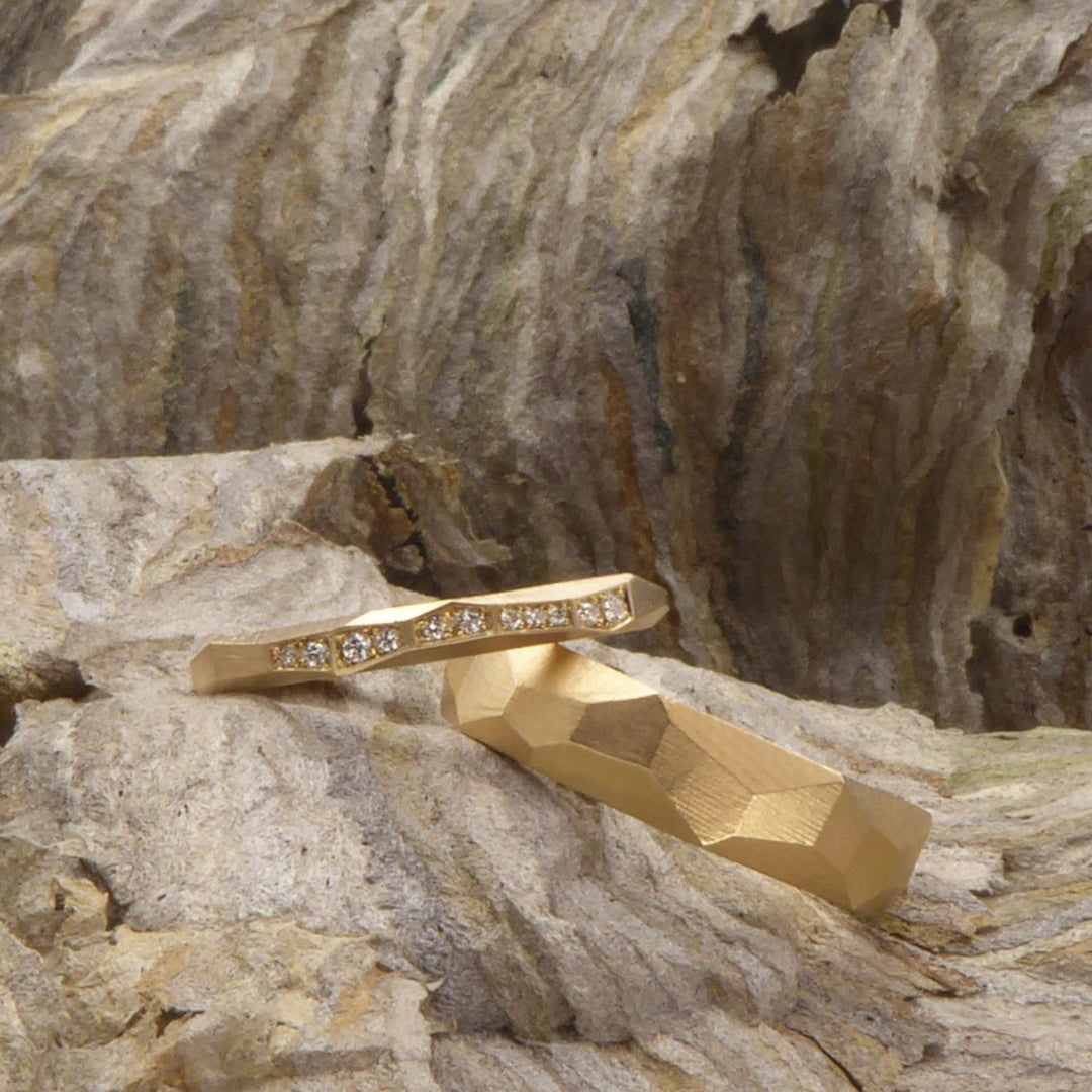 ein-paar-eheringe-mit-facetten-aus-fairtrade-gelbgold-die-ringe-sind-unterschiedlich-breit-und-der-schmalere-damenring-ist-mit-11-brillanten-besetzt