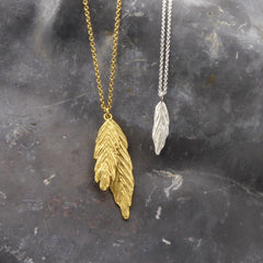 zwei-ketten-mit-feder-anhaengern-in-verschiednen-varianten-eine-kette-in-sterling-silber-mit-einem-kleinen-zarten-anhaenger-in-federform-die-andere-kette-in-vergoldetem-sterling-silber-hat-zwei-verschieden-grosse-federanhaenger-uebereinander-als-verschluss-der-ketten-in-vergoldetem-sterling-silber-ist-ein-karabiner-befestigt-den-man-auf-zwei-verschiedene-laengen-einhaken-kann-handgefertigt-in-unserer-goldschmiede-in-frankfurt-am-main