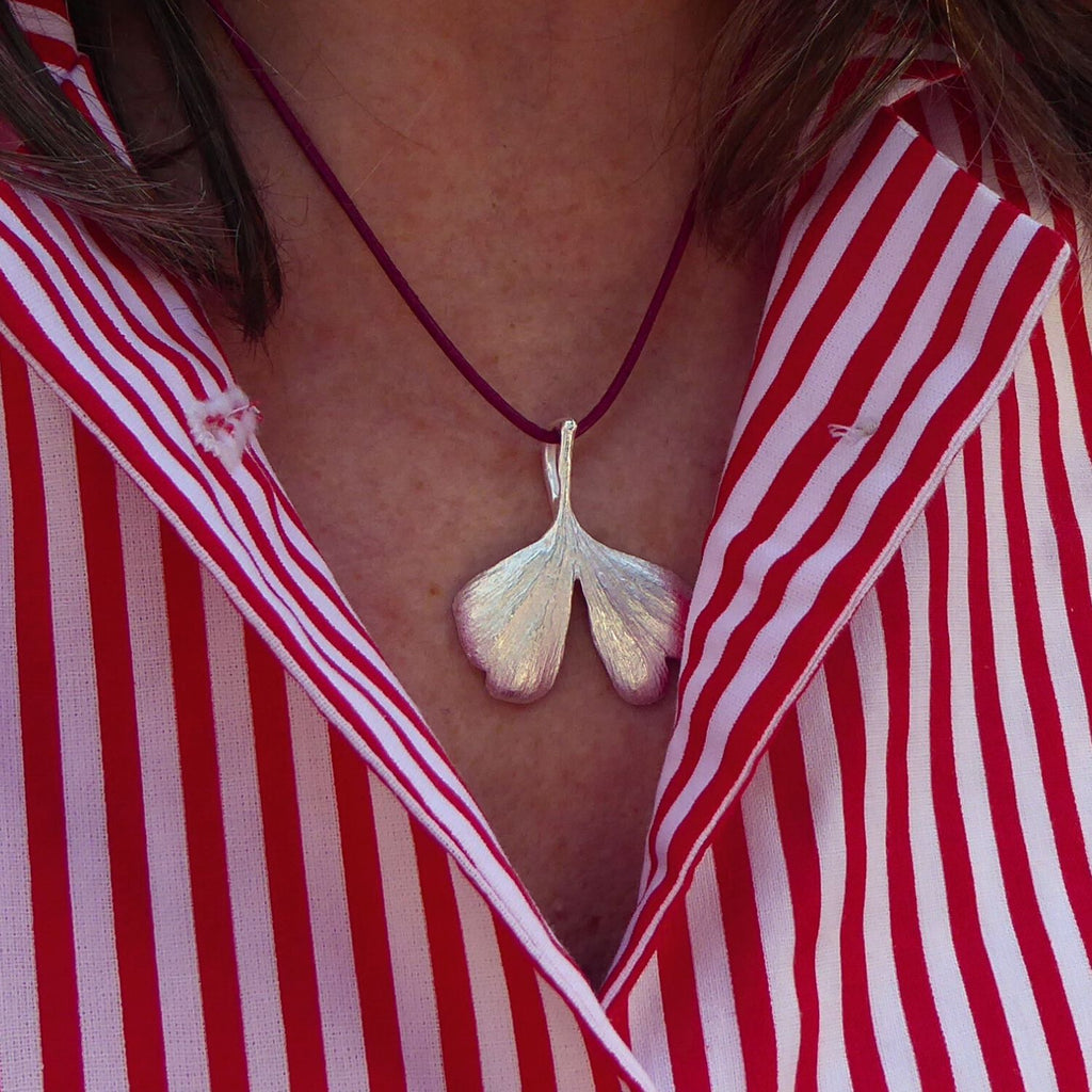 mittelgroßer-handgefertigter-ginkgo-anhänger-mit-feiner-struktur-von-echten-ginkgoblaettern-abgeformt-ohne-kette-an-lederband-getragen-in-sterling-silber-aus-unserer-goldschmiede-in-frankfurt-auch-in-fairmined-silber-erhaeltlich-geschwungene-form-mit-einem-schlitz-und-wellen-an-den-blattspitzen-ungefaehr-37-millimeter
