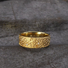 ein-gelbgoldener-ring-mit-einer-oberflaechen-struktur-die-an-eine-mond-landschaft-mit-kratern-erinnert-in-einigen-kratern-sind-brillanten-eingefasst-der-ring-ist-innen-poliert