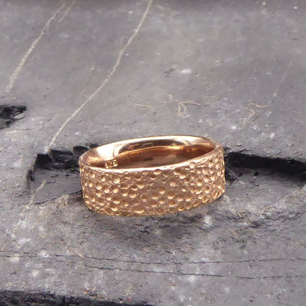 ein-rosegoldener-ring-mit-einer-strukturierten-oberflaeche-die-an-eine-mond-landschaft-mit-kratern-erinnert-der-ring-ist-innen-poliert