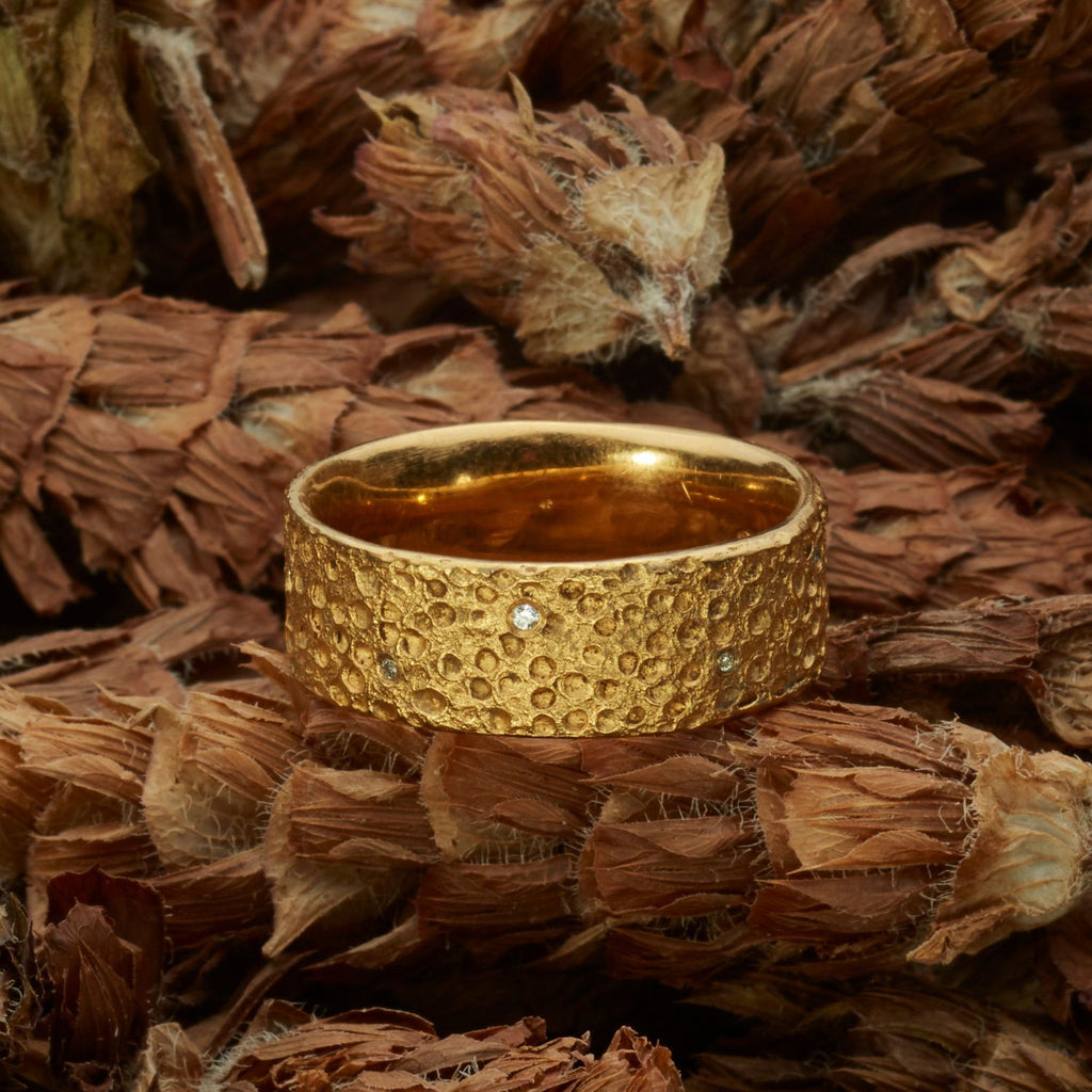 ein-gelbgoldener-ring-mit-einer-oberflaechen-struktur-die-an-eine-mond-landschaft-mit-kratern-erinnert-in-einigen-kratern-sind-brillanten-eingefasst-von-alexandra-baum-schmuck