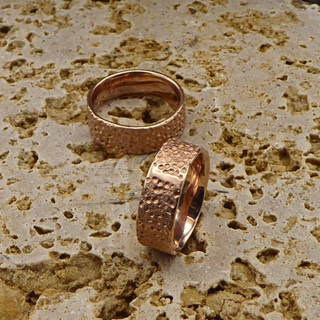 zwei-rotgoldene-ringe-mit-einer-strukturierten-oberflaeche-die-an-eine-mond-landschaft-mit-kratern-erinnert-innen-sind-die-ringe-poliert