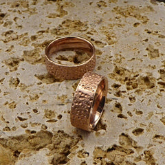 zwei-rotgoldene-ringe-mit-einer-strukturierten-oberflaeche-die-an-eine-mond-landschaft-mit-kratern-erinnert-innen-sind-die-ringe-poliert