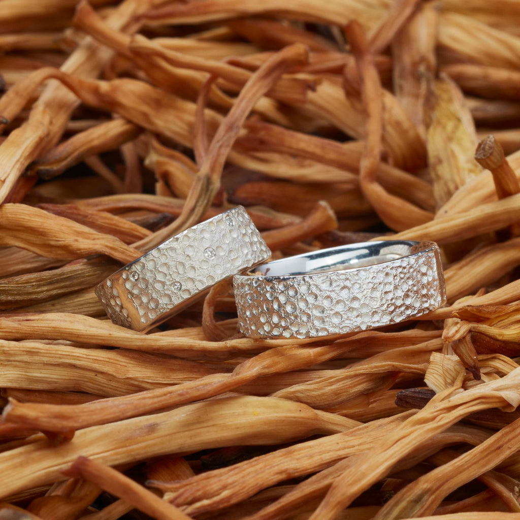 zwei-silberne-ringe-mit-einer-oberflaechen-struktur-die-an-eine-mond-landschaft-mit-kratern-erinnert-in-einigen-kratern-des-linken-ringes-sind-brillanten-eingefasst-von-alexandra-baum-schmuck-in-frankfrt