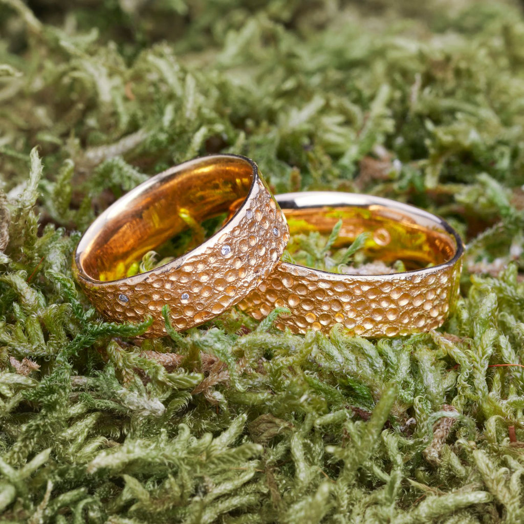 zwei-gelbgoldene-ringe-mit-einer-oberflaechen-struktur-die-an-eine-mond-landschaft-mit-kratern-erinnert-in-einigen-kratern-des-linken-ringes-sind-brillanten-eingefasst-von-alexandra-baum-schmuck-in-frankfrt