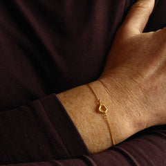 am-handgelenk-getragenes-bergsee-armband-mit-einem-kleinen-anhaenger-wie-berge-mit-einem-see-in-ihrer-mitte-statt-des-sees-ist-in-der-mitte-des-anhaengers-ein-reizvolles-loch-durch-das-man-durchgucken-kann-als-verschluss-des-armbands-in-vergoldetem-sterling-silber-ist-ein-karabiner-befestigt