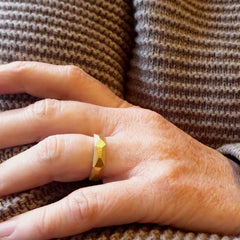 ein-an-der-hand-getragener-schmaler-ring-mit-vielen-unregelmaessigen-facetten-beziehungsweise-polygonen-flaechen-der-ring-ist-ca-viereinhalb-millimeter-breit-und-besteht-aus-gelbgold-er-ist-auch-in-fairtrade-gold-erhaeltlich-und-individualisierbar-die-ringe-werden-von-hand-in-unserer-goldschmiede-in-frankfurt-am-main-angefertigt-alexandra-baum-schmuck