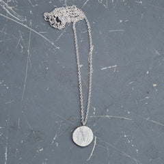 gras-anhaenger-kette-mit-einem-runden-anhaenger-mit-der-struktur-von-abgeformtem-gras-auf-dem-bild-ist-die-kleinere-variante-zu-sehen-die-kette-besteht-aus-recycling-sterling-silber-als-verschluss-der-kette-ist-ein-karabiner-befestigt-den-man-auf-zwei-verschiedene-laengen-einhaken-kann-nachhaltiger-schmuck-von-hand-gefertigt-in-unserer-goldschmiede-werkstatt-in-frankfurt-bockenheim-alexandra-baum-schmuck